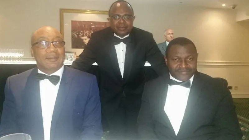 Three men in black tie pose for a photograph at their dinner table.