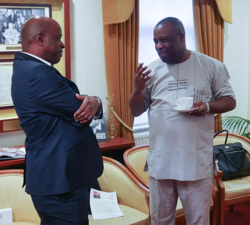 Two delegates, one in Nigerian traditional attire, chat over cups of tea.