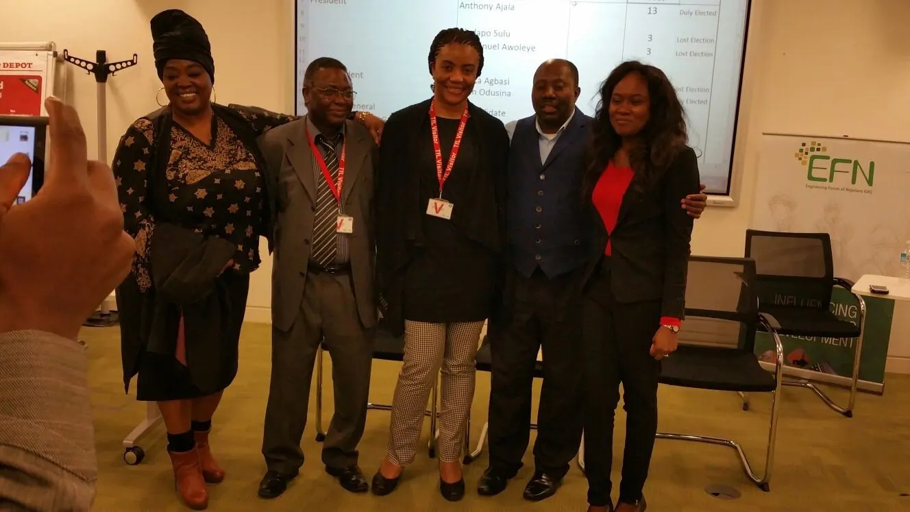 Five participants wearing lanyards pose in front of a presentation screen beside an EFN banner.