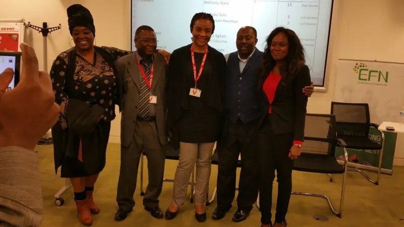 Five participants wearing lanyards pose in front of a presentation screen beside an EFN banner.