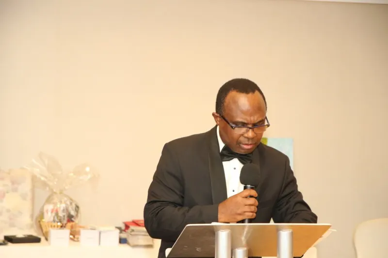 A speaker in black tie addresses the guests from a lectern.