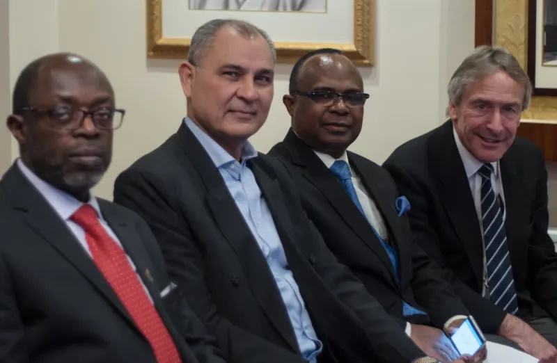 Four delegates in suits seated in a row, smiling towards the camera.