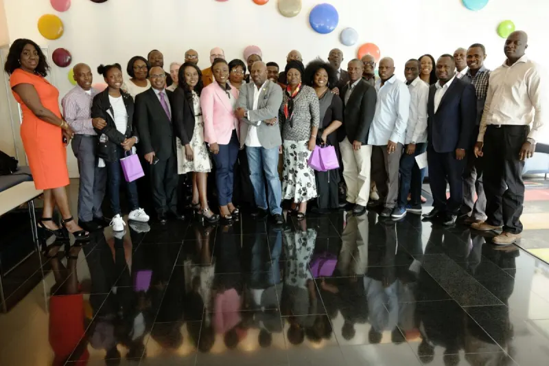 A large group of participants lines up for a group photograph in a bright atrium with a polished floor.
