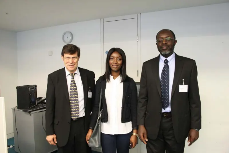 Three delegates, two men in suits and a woman, pose together in the conference room.
