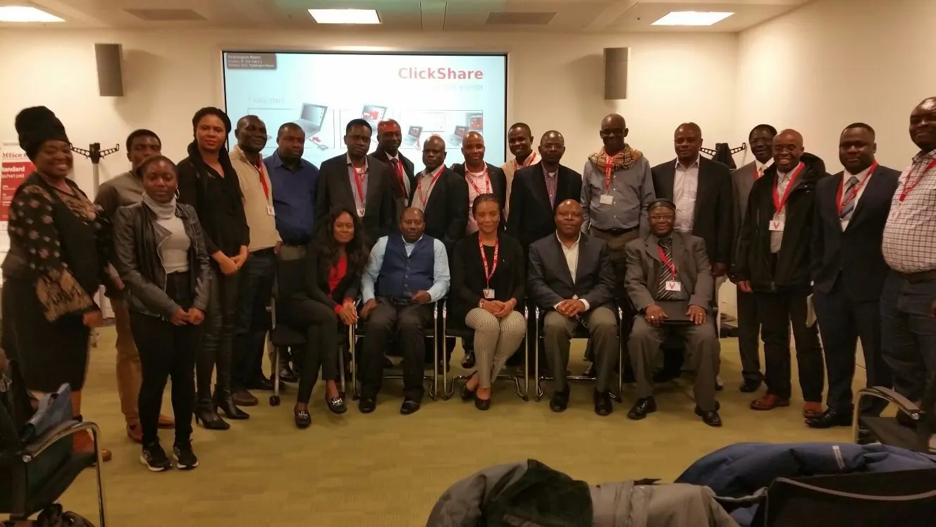 Group photograph of around thirty workshop participants, some seated and some standing, in front of a presentation screen.