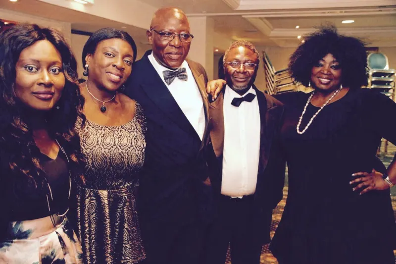 Five guests in evening wear, two of the men in bow ties, pose together smiling.