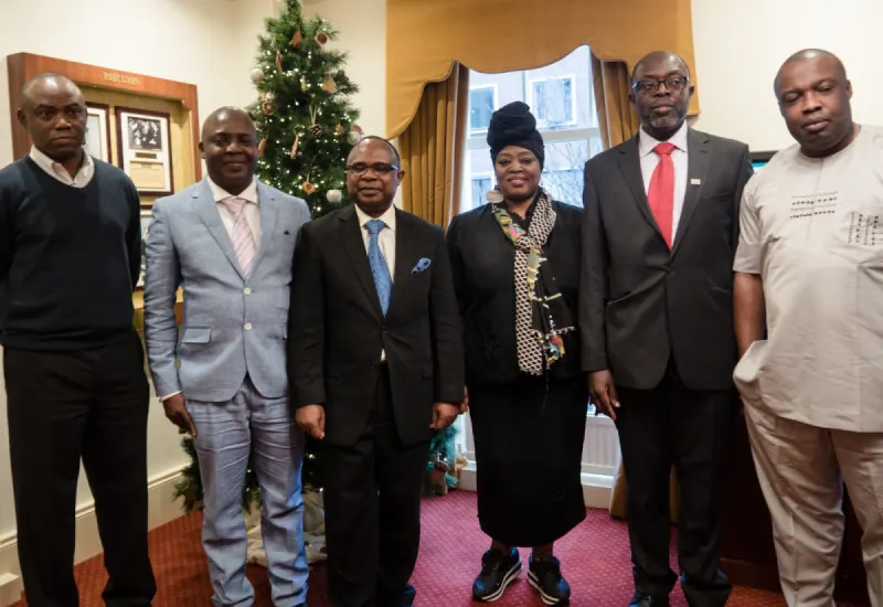 Six delegates, in suits and Nigerian traditional dress, pose in front of a Christmas tree.