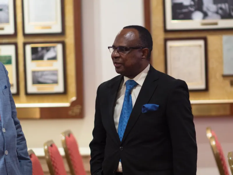 A delegate in a dark suit and blue tie in a room lined with framed historic photographs.