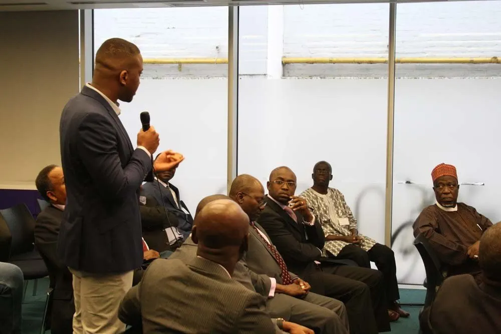 A delegate stands with a microphone to put a question to the panel while the audience listens.